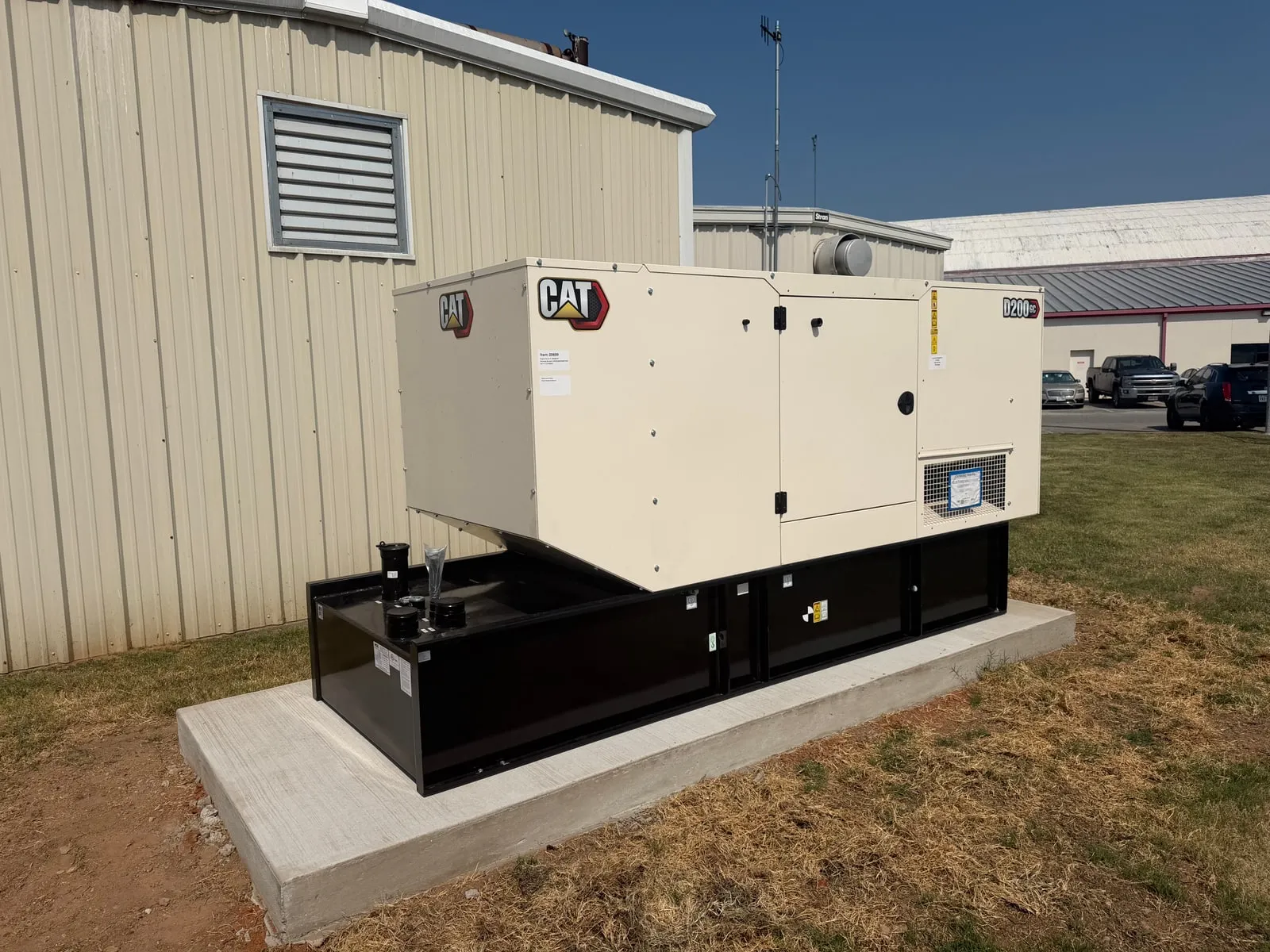 A CAT standby generator set installed on a concrete pad beside a metal building, with its fuel tank base and exterior control panel visible.